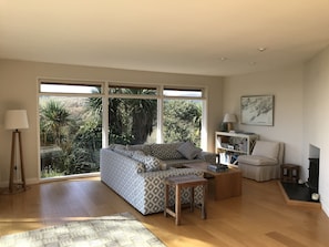 A spacious living room with a large window, a sofa, a coffee table, a lamp, and a bookshelf. - Private waterfront house with its own 3 acres sloping to the sea (Tralispean)