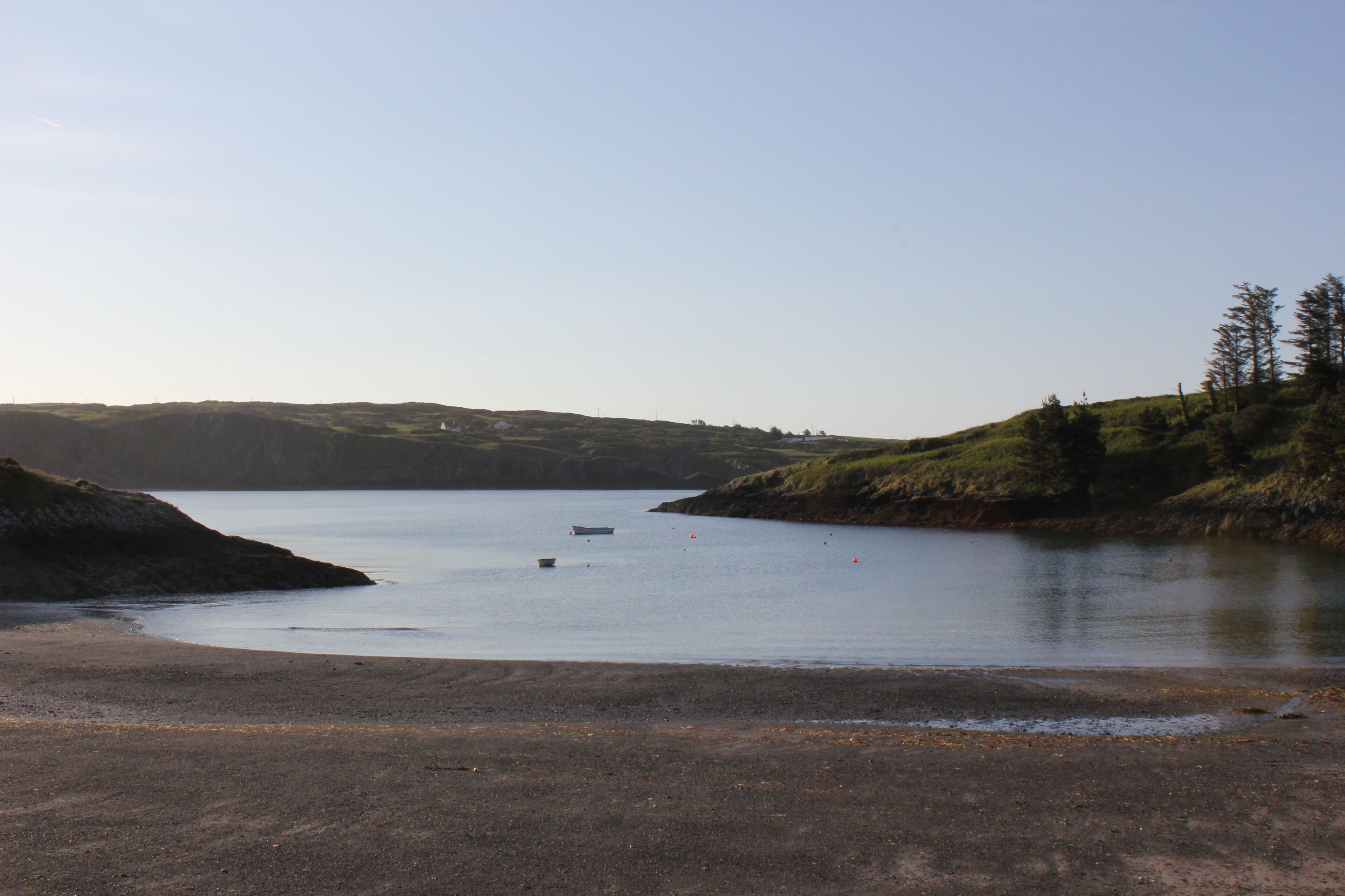 A calm lake with a boat, surrounded by grassy hills and a clear sky.