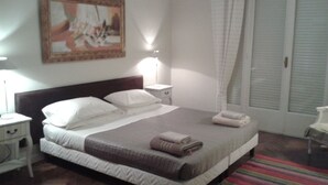 Ein ordentlich bezogenes Bett mit Kissen und Decke, ein Nachttisch mit Lampe, ein Sessel und ein Bild an der Wand.