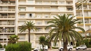 Ein mehrstöckiges Hotel mit Balkonen, geparkten Autos und Palmen.