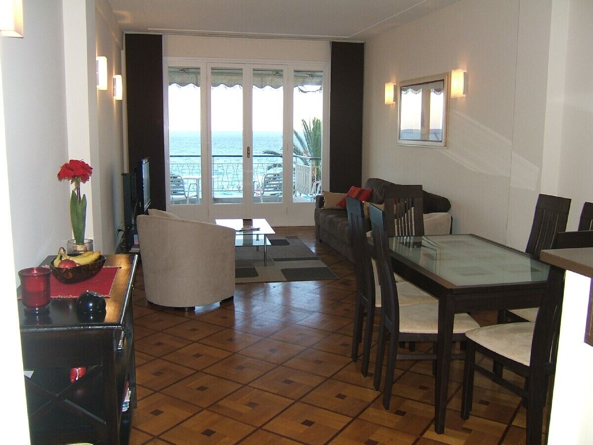 A living room with a glass table, chairs, a sofa, and a view of the sea through large windows.