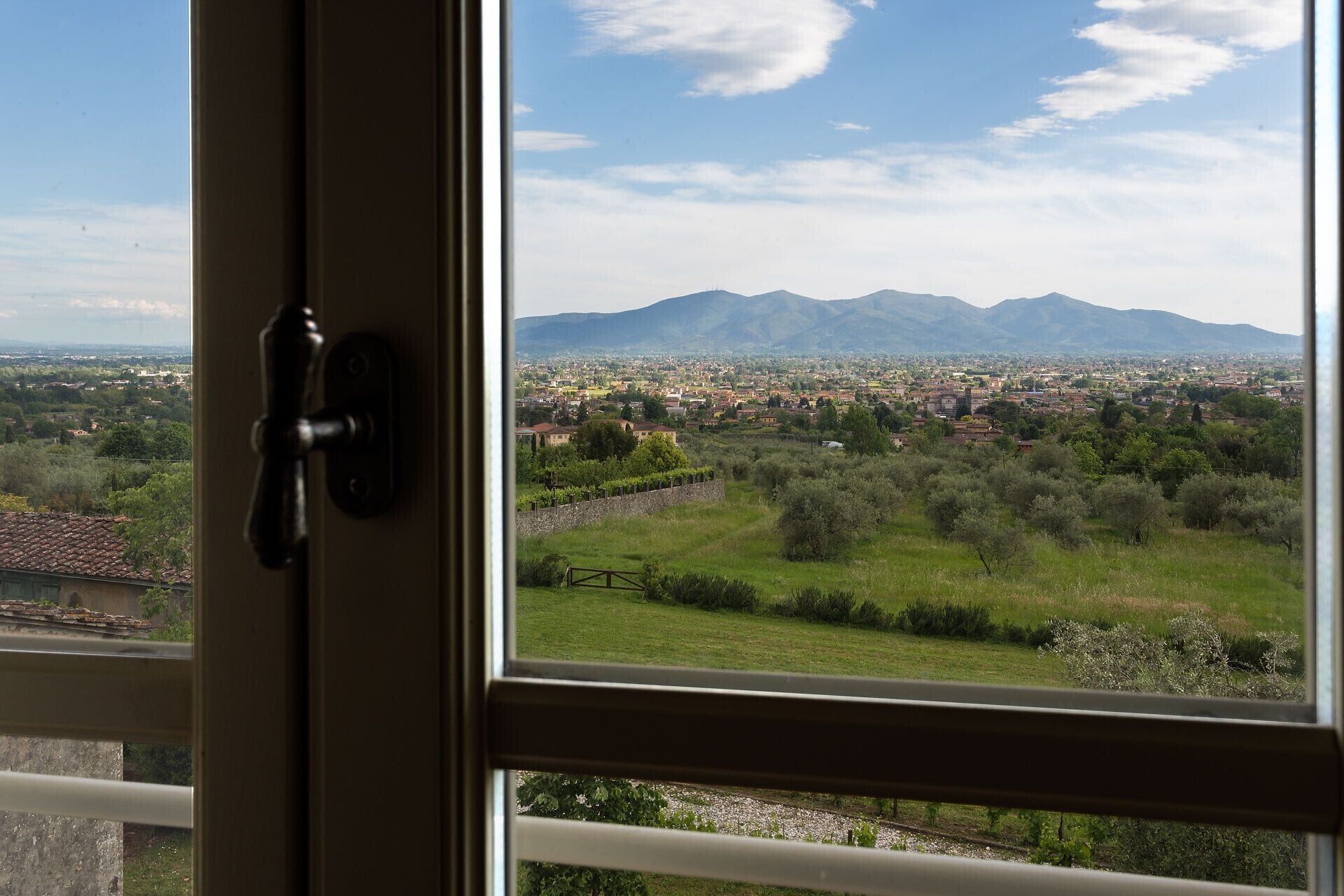 Blick durch ein Fenster mit Türgriff, zeigt eine Stadtansicht mit Bergen im Hintergrund.