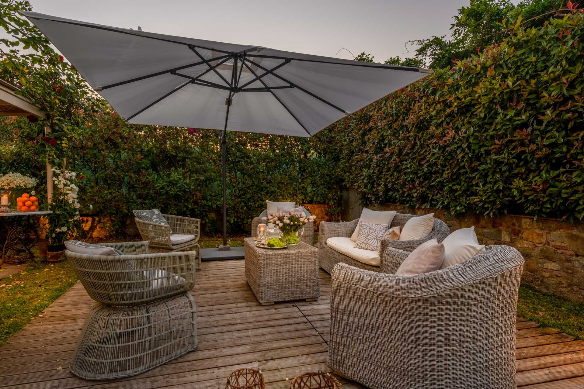 An outdoor patio with wicker furniture, a large umbrella, and a wooden deck.