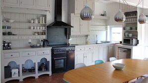 A modern kitchen with white cabinetry, a black range hood, stainless steel appliances, and pendant lighting. - Stunning views of Snowdonia Mountains (Near Caernarfon)