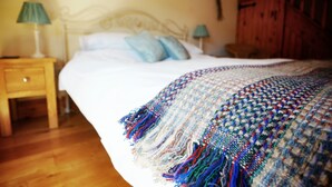 Une chambre à coucher avec un lit recouvert d’une couverture tissée aux couleurs vives, une table de chevet en bois avec une lampe et une armoire en bois.