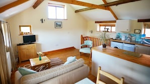 Une pièce chaleureuse avec un plafond en bois, un canapé, une télévision, une table à manger et un coin cuisine équipé d’un évier et de placards.