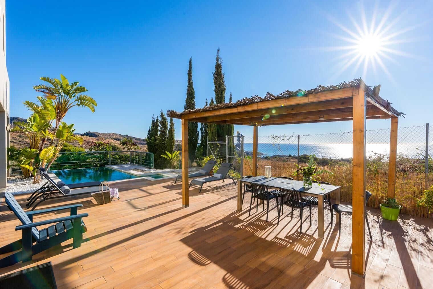 Une terrasse en bois avec une piscine, des chaises longues et une pergola offrant une vue sur la côte.