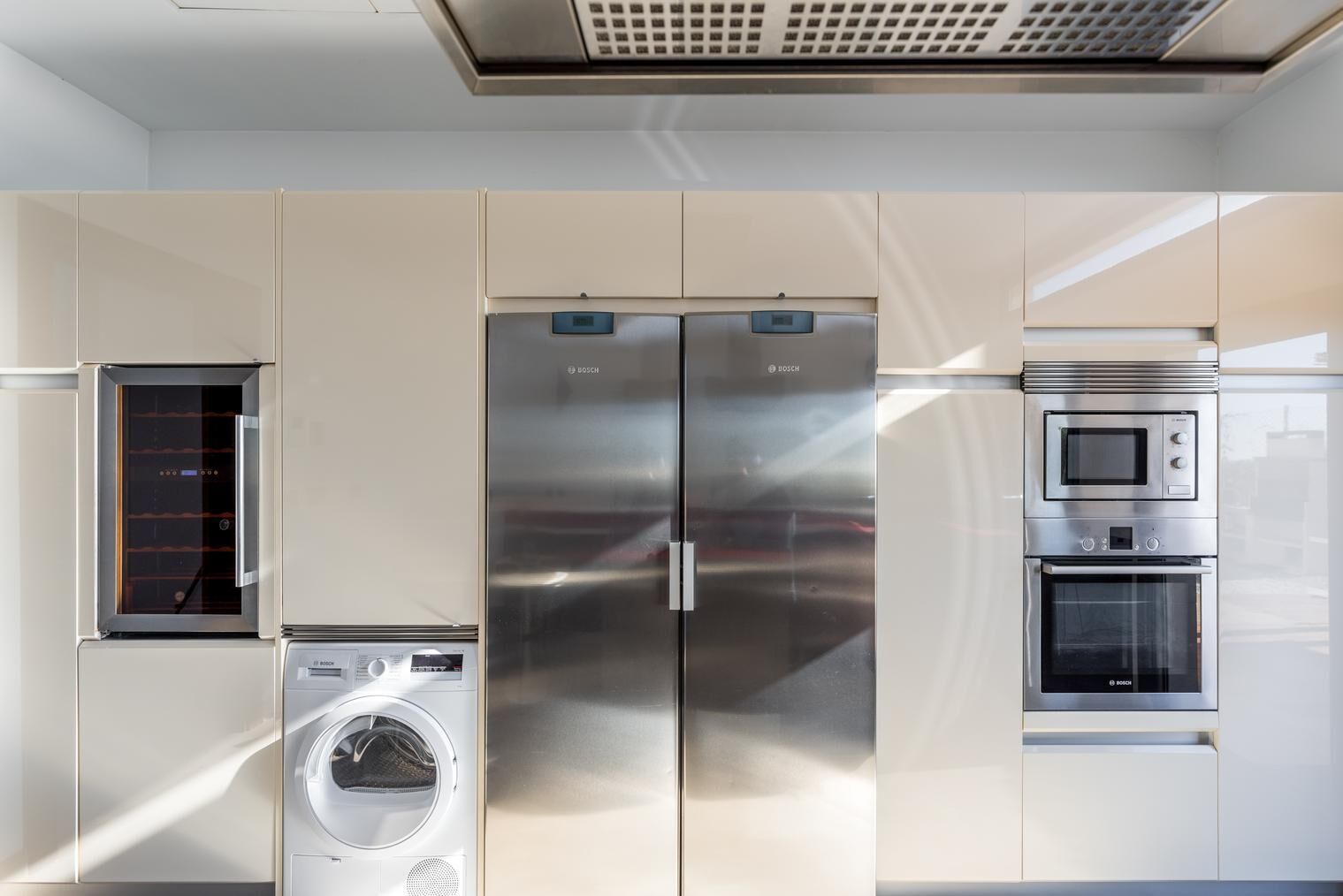 A modern kitchen with stainless steel appliances, including a double-door refrigerator, a built-in oven, and a washing machine.