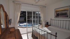 Une chambre dotée d’un grand lit, d’une commode en bois, d’un ventilateur de plafond et offrant une vue sur une piscine extérieure.