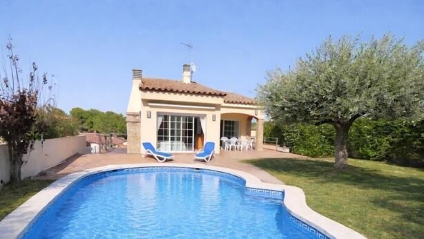 Une piscine avec deux chaises longues, une maison avec un toit en tuiles et un arbre en arrière-plan.