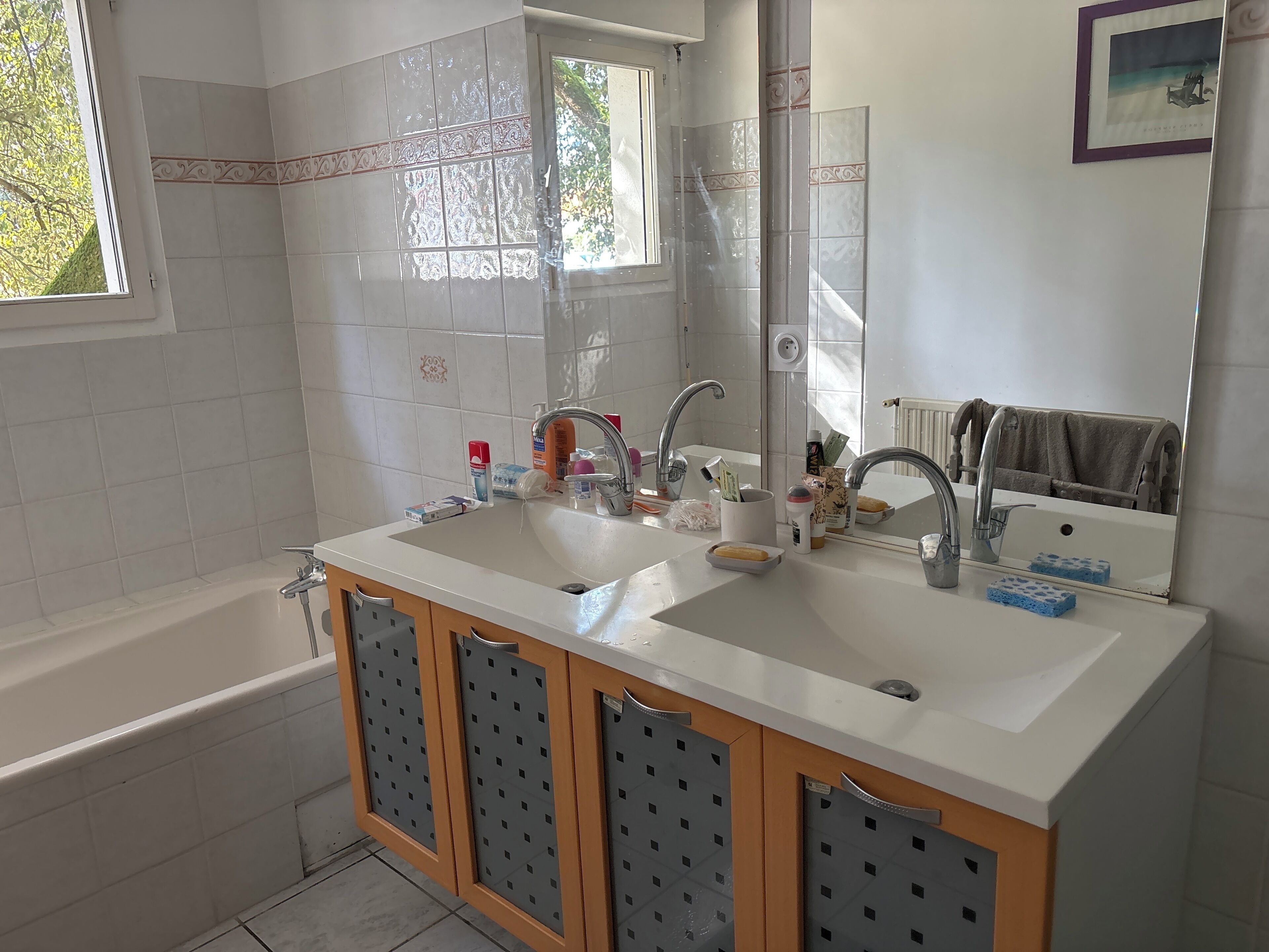 A bathroom with a double sink, a bathtub, and a large mirror.