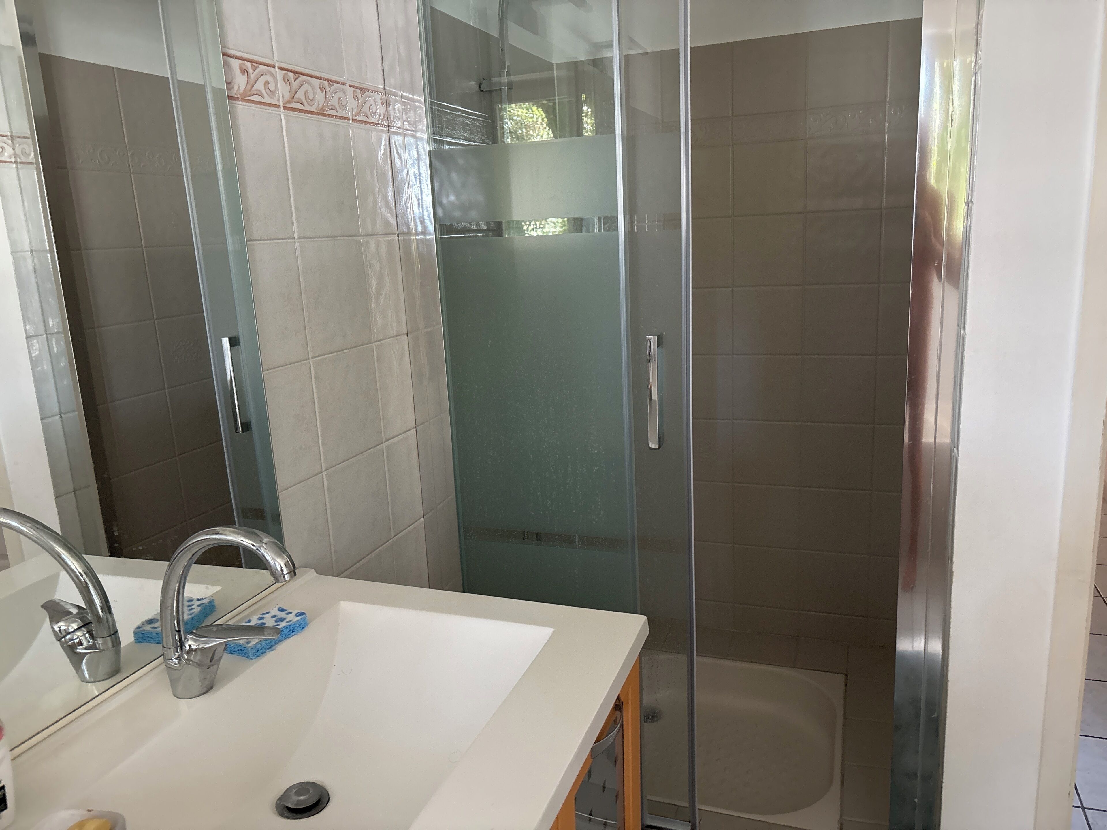 Une salle de bain avec un lavabo blanc, une cabine de douche en verre et une zone de douche carrelée.