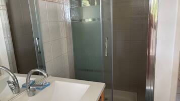 Een badkamer met een witte wastafel, een douchecabine van glas en een betegelde douche.