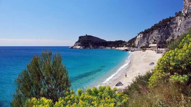 A coastal beach with clear blue waters, a rocky cliff, and a small building on the shore. - Apartment with wonderful terrace on the sea - Finale Ligure (Finale Ligure)