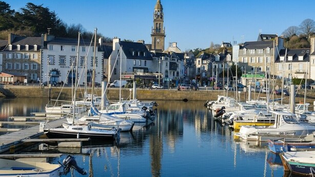 En lystbådehavn med flere både i havnen, et markant klokketårn og historiske bygninger i baggrunden.