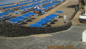 Ein Strand mit Reihen blauer Sonnenschirme und Liegen.