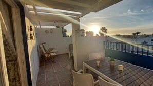 Ein Balkon mit Holztisch und Stühlen, Blick aufs Meer und eine weiße Wand mit einer Uhr und Dekoration.