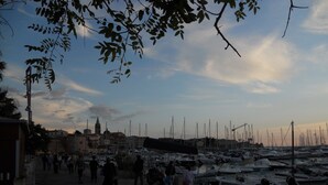 Ein Yachthafen mit vertäuten Booten, eine Stadt im Hintergrund und Menschen, die am Ufer entlanggehen.