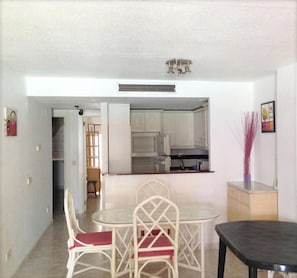 A compact kitchen with white cabinets, a dining area with a round table and chairs, and a small cabinet to the side.