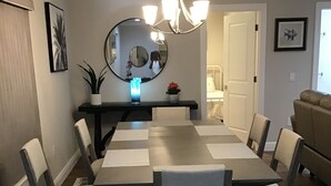 Une salle à manger avec une table rectangulaire, six chaises, un lustre, un miroir rond et une petite plante posée sur une console.