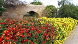 A stone bridge with an arch over a pathway lined with vibrant red and yellow flowers. - WAKE UP TO THE SOUND OF THE SEA T1 CENTRAL-AIR CONDITIONING(FREE WIFI) 3' BEACH (Luz)