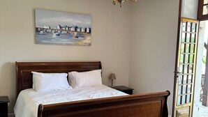 Un dormitorio con una cama de madera, un cuadro de un puerto, una araña y una puerta que da al exterior.