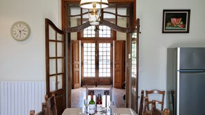 Un comedor con una mesa dispuesta para cuatro, una araña, sillas de madera, un reloj y un refrigerador.