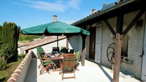 Un patio al aire libre con una mesa, sillas, un paraguas verde y vistas al campo.
