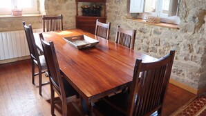 Une table à manger en bois, accompagnée de six chaises, un mur en pierre et une fenêtre avec des volets.