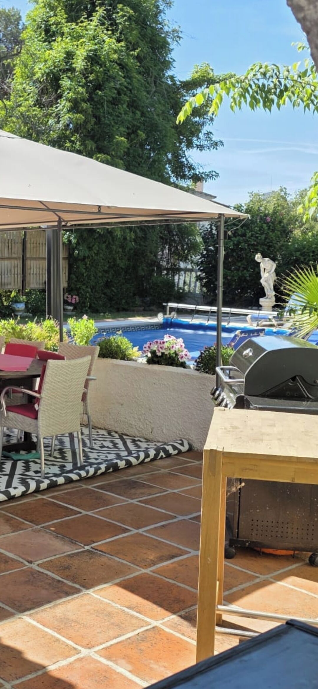 Un espace extérieur aménagé en patio, avec un coin salon couvert, un barbecue et une piscine.