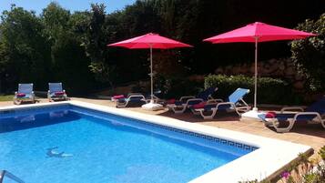 Une piscine avec des chaises longues et des parasols rouges.