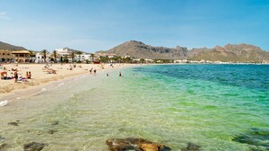 A beach with clear turquoise water, people sunbathing, and buildings in the background. - GARROVERA - Beautiful Finca for 8 persons in Pollensa (Pollensa / Pollença)