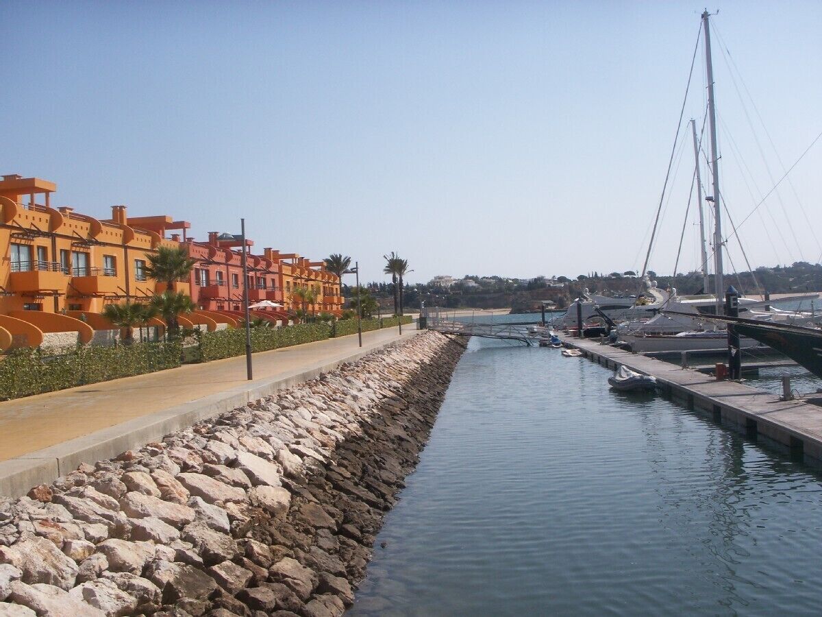 A marina with boats docked, a stone seawall, and colorful buildings along the waterfront.