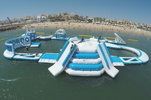 An inflatable water park with slides and play structures in the water, surrounded by a beach and buildings in the background. - Luxury T1 in Portimão (Portimão)