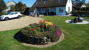 A house with a gravel driveway, a lawn with a flower bed, and a parked car. - Architect Designed Stunning House, In Quiet And Peaceful Stunning Location  (Tenby. Pembrokeshire)