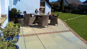 An outdoor patio with wicker furniture, a table, and an umbrella. - Architect Designed Stunning House, In Quiet And Peaceful Stunning Location  (Tenby. Pembrokeshire)