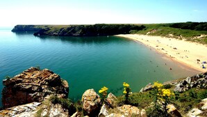 A coastal beach with rocky cliffs and clear blue water. - Architect Designed Stunning House, In Quiet And Peaceful Stunning Location  (Tenby. Pembrokeshire)