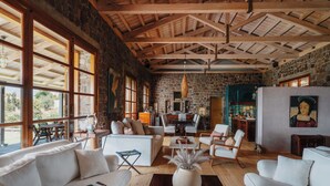 A spacious living area with a stone wall, wooden ceiling beams, and large windows. - Luxury Prinate Villa in Aegina (Aegina)