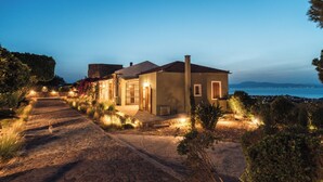 A house with a paved driveway leading to the entrance, surrounded by landscaped gardens and a view of the sea. - Luxury Prinate Villa in Aegina (Aegina)