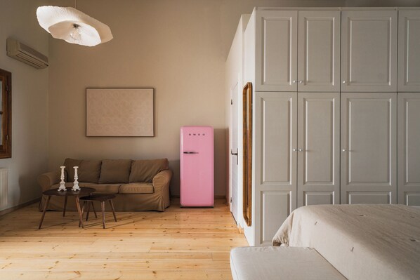 A room with a wooden floor, a beige sofa, a pink refrigerator, a white wardrobe, and a hanging light fixture. - Luxury Prinate Villa in Aegina (Aegina)