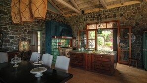 A rustic kitchen with stone walls, wooden ceiling beams, and a large island with a sink. - Luxury Prinate Villa in Aegina (Aegina)
