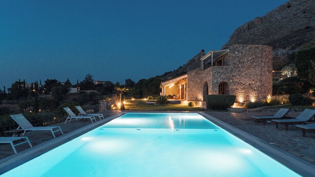 A swimming pool with lounge chairs, a stone building with arched windows, and a mountainous backdrop. - Luxury Prinate Villa in Aegina (Aegina)