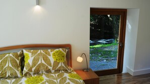Un dormitorio con una cama, una mesita de noche, una lámpara y una puerta que da a un jardín.