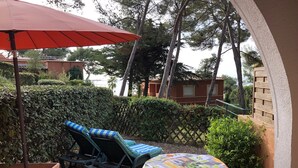 A patio area with a table and chairs, a red umbrella, and a view of a building and trees. - Flat - 2 rooms - 4 persons (Sanary-Sur-Mer)