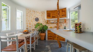 A modern kitchen with a stone wall, wooden cabinets, a large island, and a dining area with white chairs. - Villa CASA VERDE with private parking and swimming pool. WIFI, A/C, Terraces and BBCOA⭐⭐⭐⭐⭐ (sant francesc)