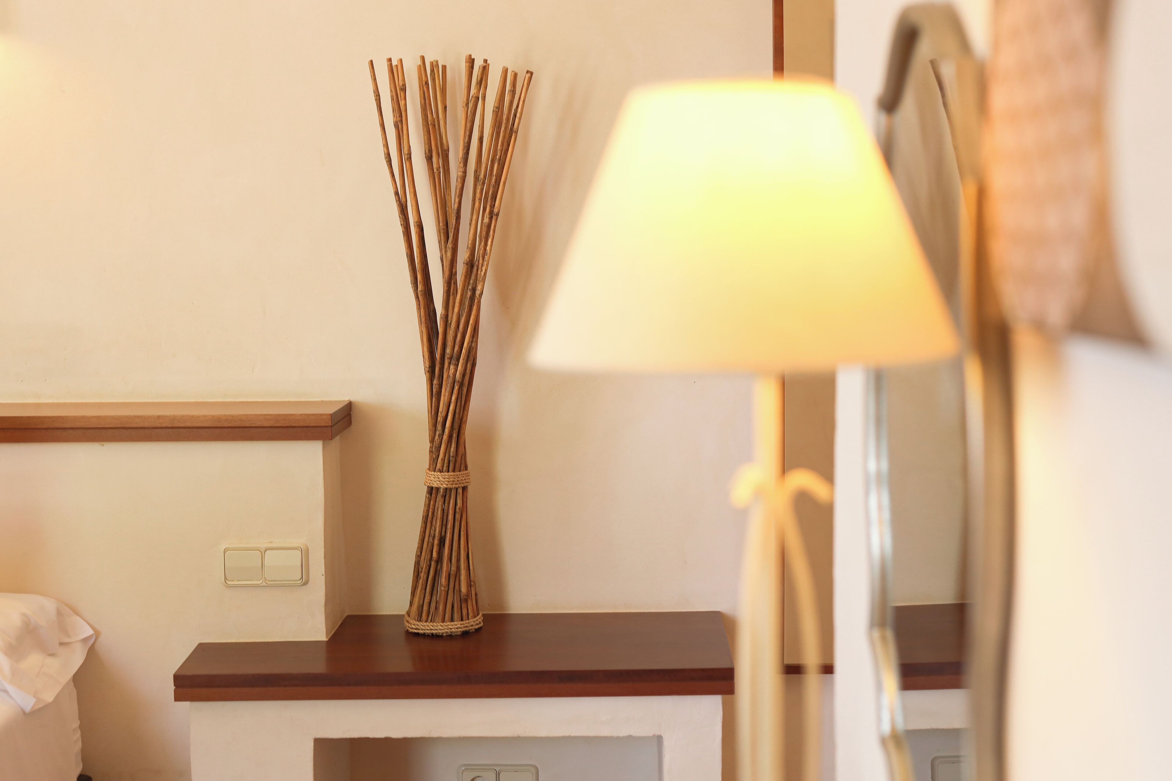 A hotel room with a wooden bedside table, a lamp, and a wall-mounted light switch.