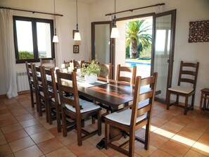 Un área de comedor con una mesa y sillas de madera, una planta en maceta y vistas a una piscina a través de un ventanal.