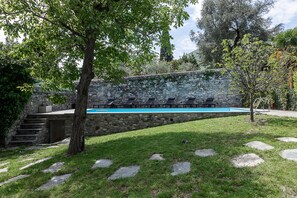 A stone wall with a swimming pool and lounge chairs.
