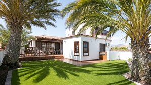 Una casa con un patio, un jardín pequeño y palmeras.