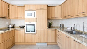 Una cocina moderna con armarios de madera, horno empotrado, microondas y pileta de acero inoxidable.